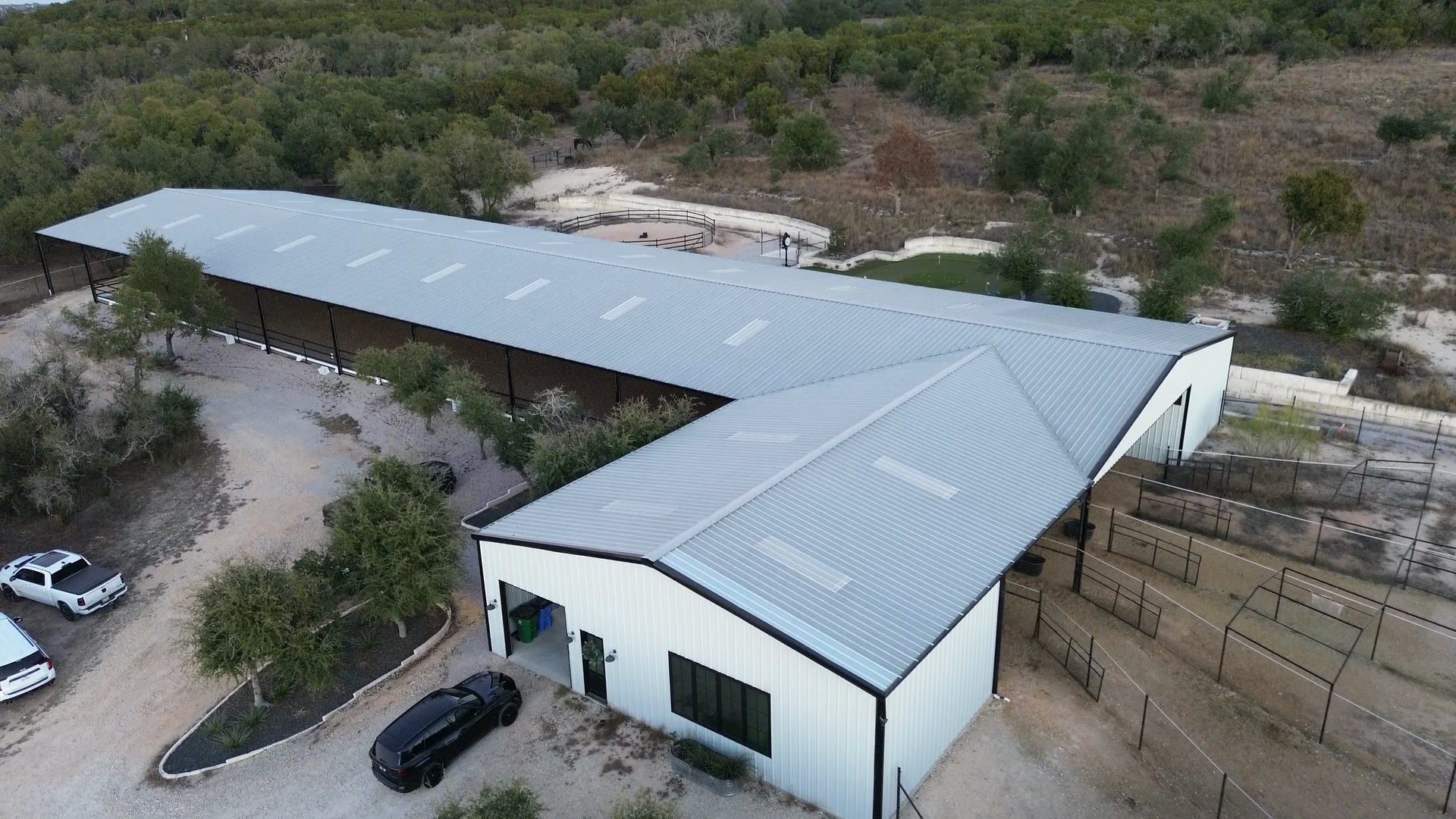 The front of the barn from the air: its white gable end and doors, with the long covered wing running back behind it