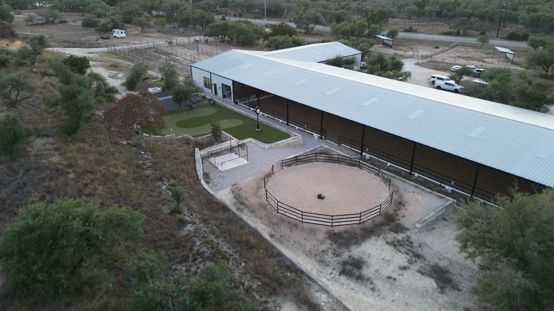 The barn, its long covered wing and the grounds beside it, from above in the evening